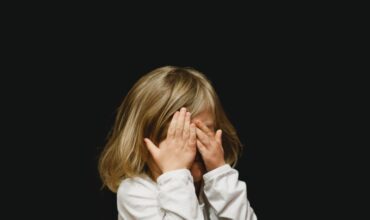 Une petite fille se couvrant les yeux sur un fond noir