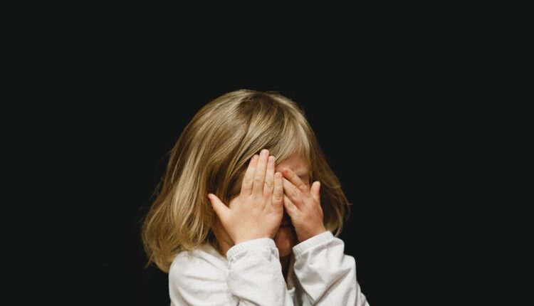 Une petite fille se couvrant les yeux sur un fond noir